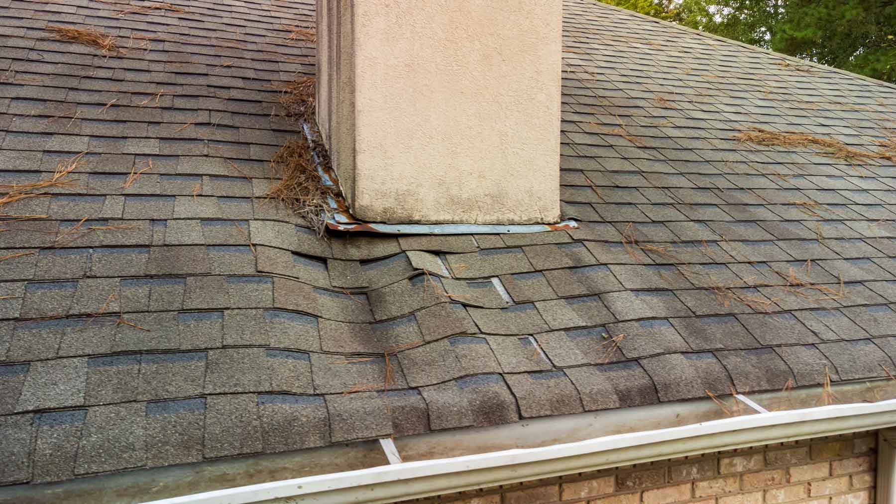 Roof with overly-saturated and damaged asphalt shingles around the chimney.