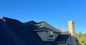 House with dark shingles and stone chimney under clear blue sky. 