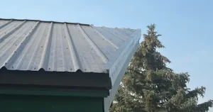 Corrugated metal roof corner of a structure with a tree under a clear sky in the background. 