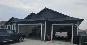 A house with an open two-car garage containing a truck, alongside a parked SUV and trash cans.