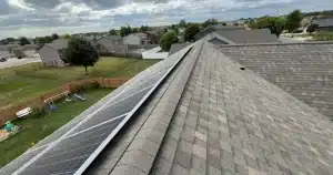 Solar panels on a house roof with a suburban background under a cloudy sky. 