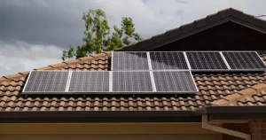 Solar panels installed on a tiled house roof under a cloudy sky.