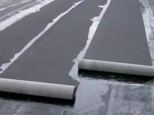 Close-up of black roofing felt rolled out on a surface, with some wet patches, ready for installation on a roof.