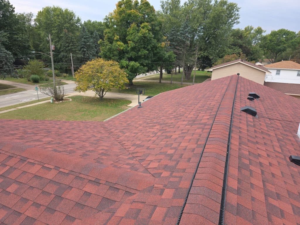 Red asphalt shingle roof on a residential home with ridge vent and surrounding neighborhood view